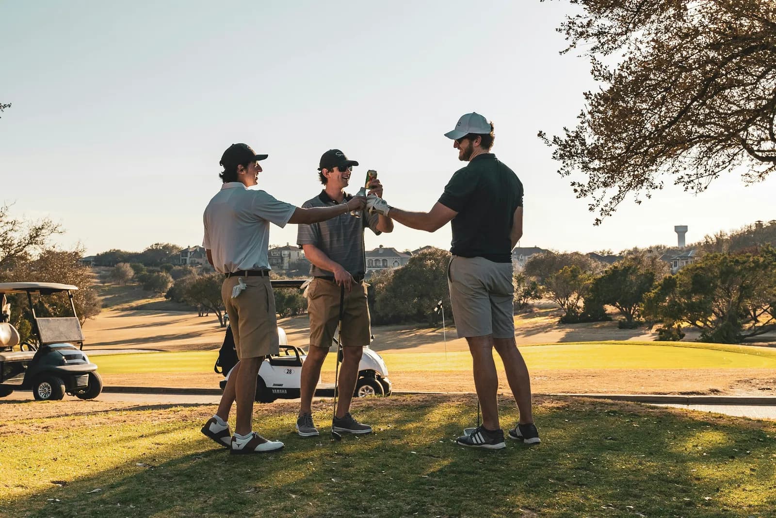 Trois golfeurs trinquant sur le parcours au coucher du soleil, voiturettes en arrière-plan