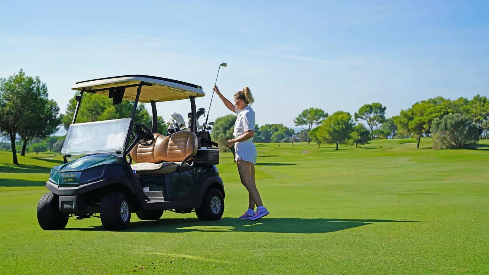 Golfeuse prenant un club à côté d'une voiturette sur un parcours ensoleillé
