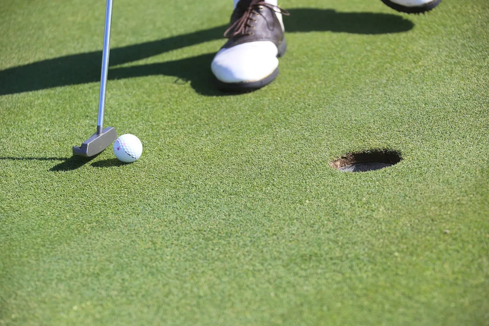 Putter posé derrière une balle de golf blanche sur un green, à quelques mètres du trou