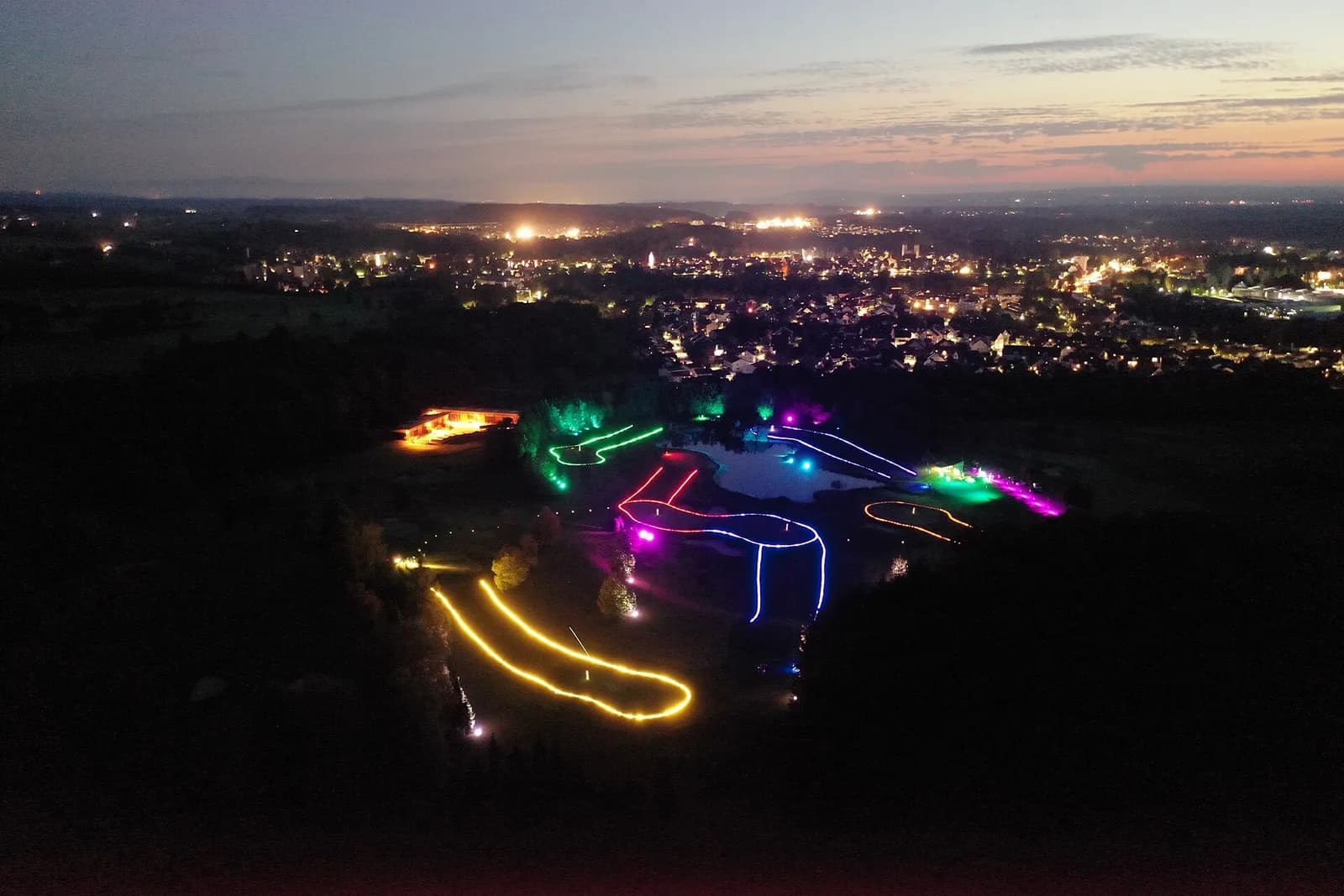 Parcours de golf de nuit balisé par des lignes de lumière colorées, vu du ciel au crépuscule