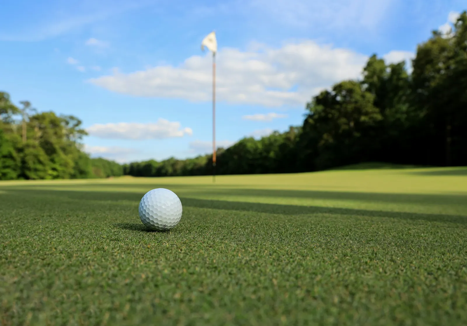 Balle de golf posée sur le fairway devant le drapeau du green