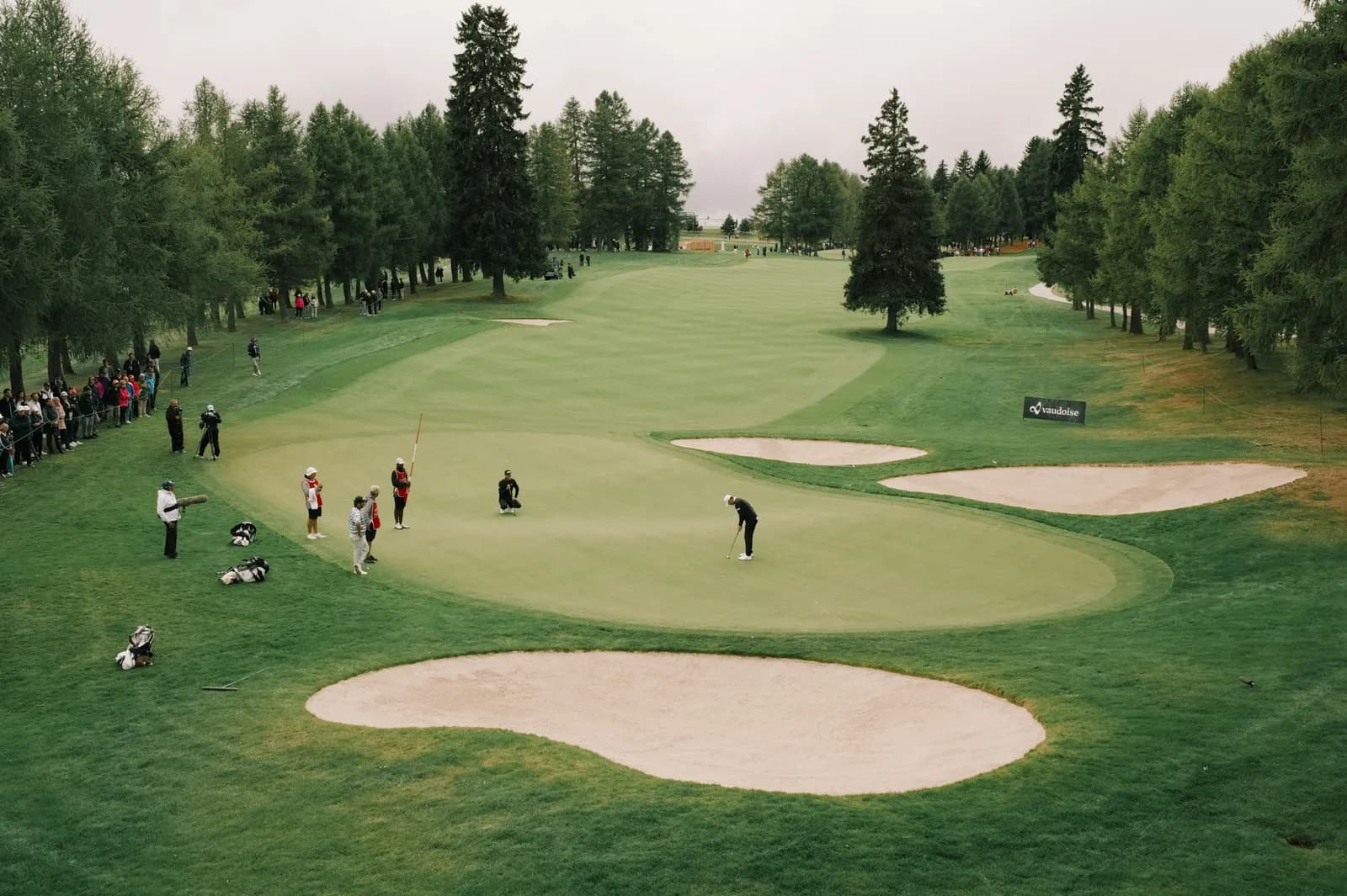Joueurs et spectateurs autour d'un green bordé de bunkers pendant une compétition de golf