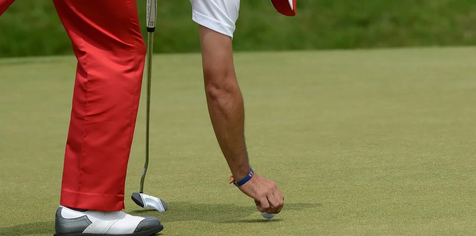 Golfeur penché sur le green qui pose son marque-balle derrière sa balle, putter à la main