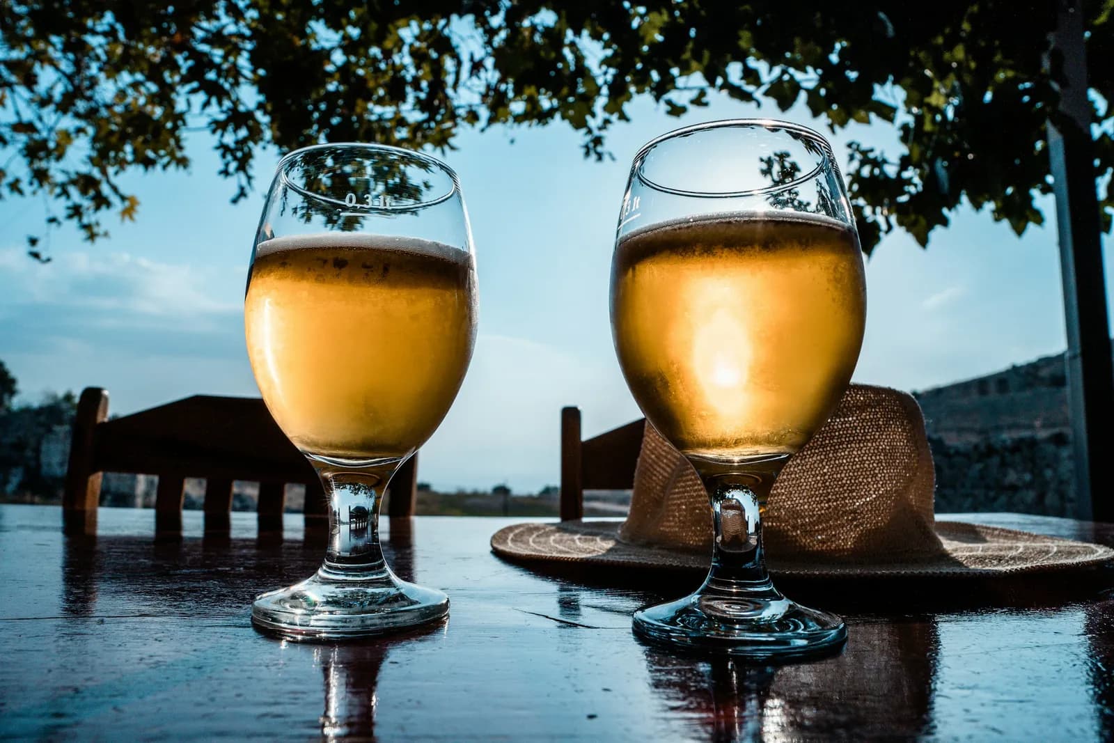 Deux verres de bière posés sur une table en terrasse sous les arbres