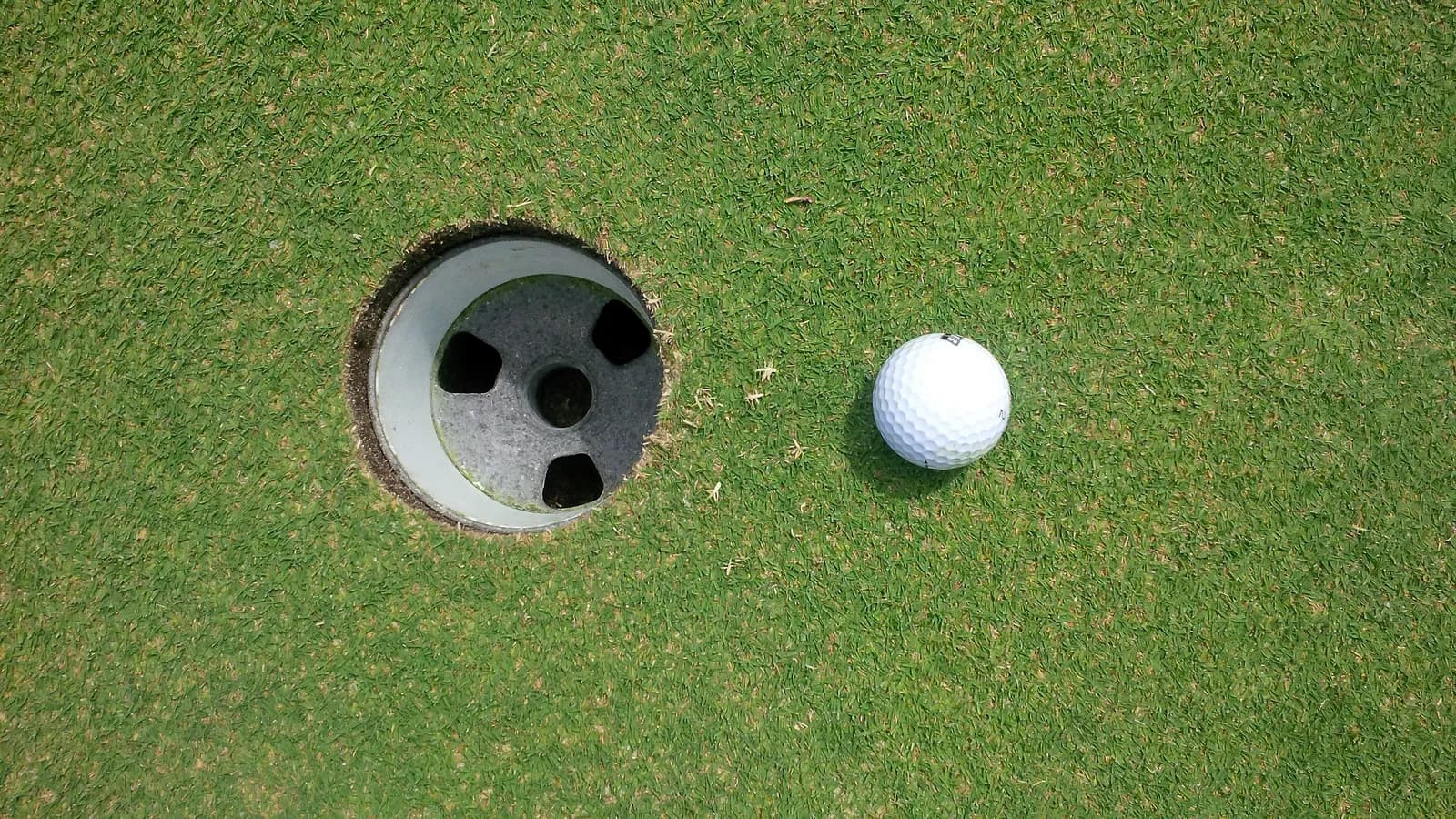 Balle de golf blanche posée sur le green à quelques centimètres du trou, vue de dessus