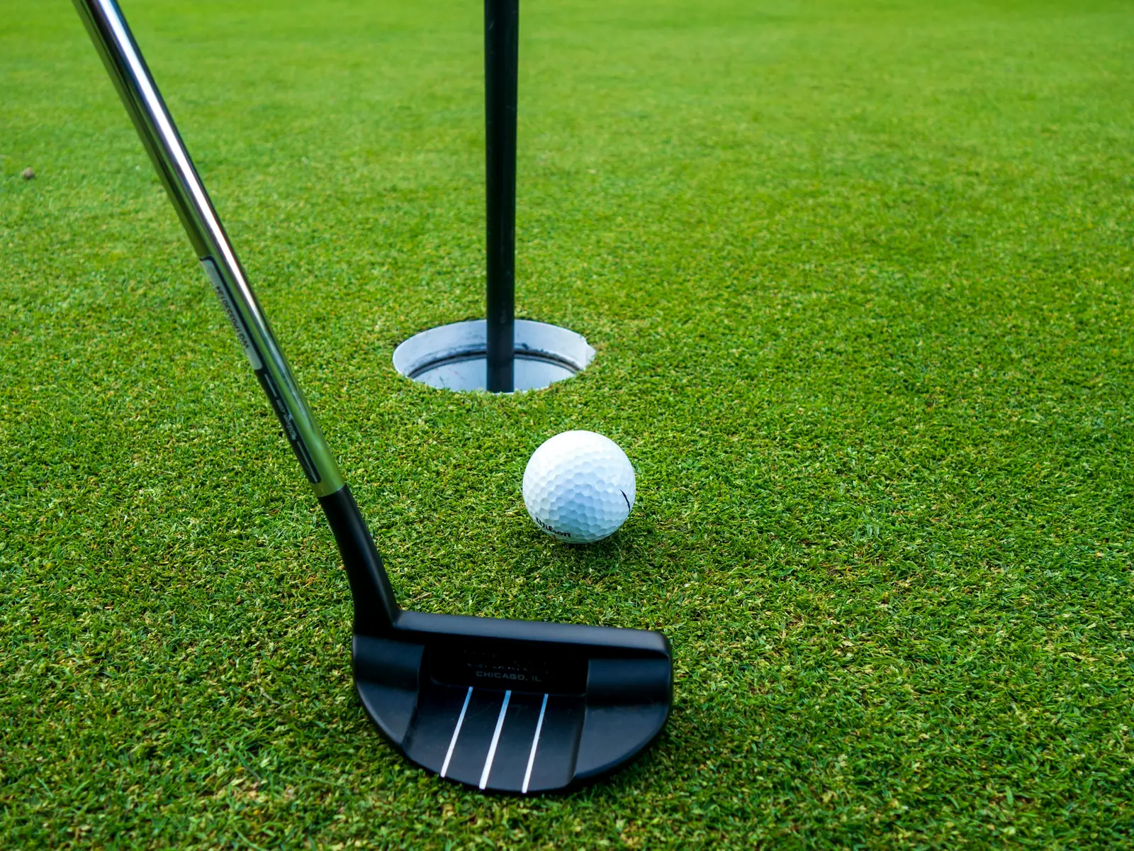 Putter et balle de golf sur le green, à quelques centimètres du trou