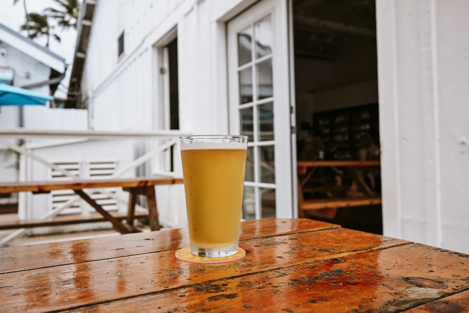Verre de bière posé sur une table en bois mouillée devant un clubhouse blanc