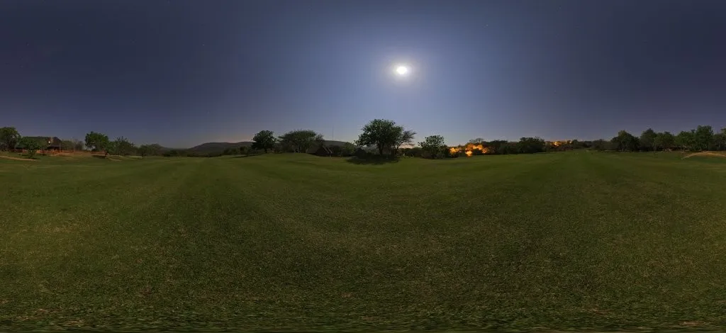 Fairway de golf sous la pleine lune, avec une rangée d'arbres et quelques lumières à l'horizon